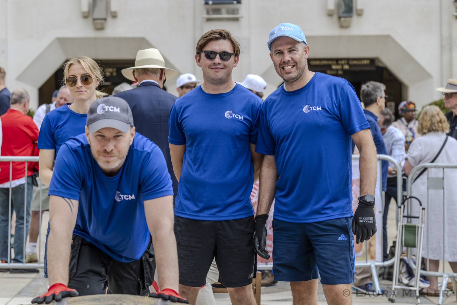 Four racers from headline sponsor TCM IP Services in blue team shirts and caps pose with their cask outside the Guildhall Art Gallery entrance, one crouched at the barrel in red-palmed gloves and three standing behind.